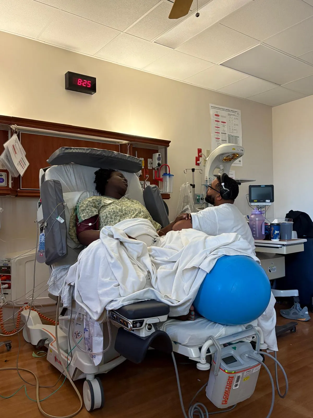 A mother in labor in a hospital bed with a birth ball while her partner comforts her