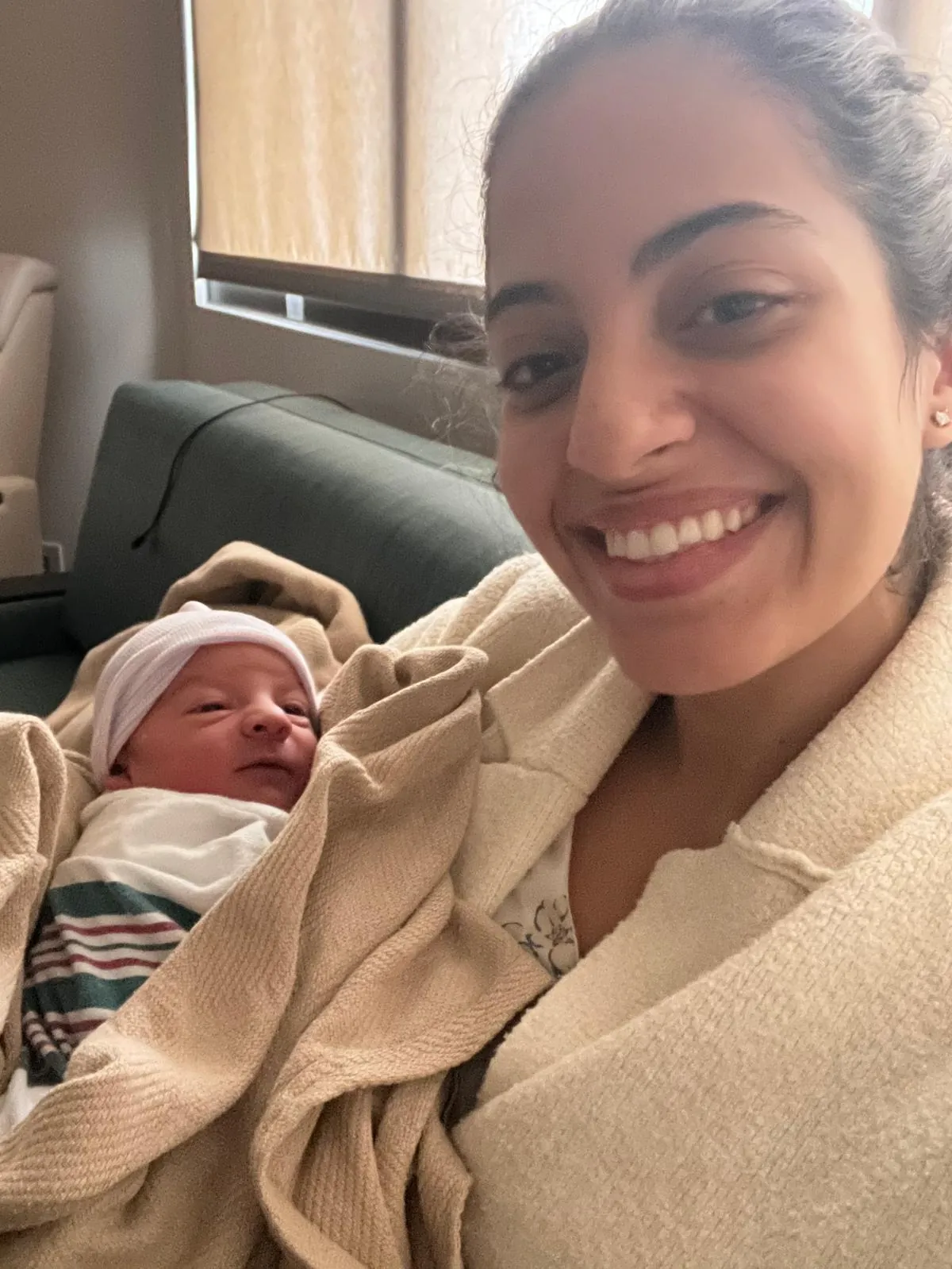 A smiling doula with a newborn wrapped in a hospital blanket beside her
